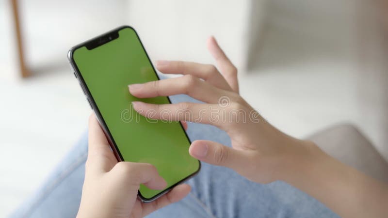 Mulher asiática segurando a mão e assistindo usando um celular inteligente com tela verde para seu próprio conteúdo personalizado