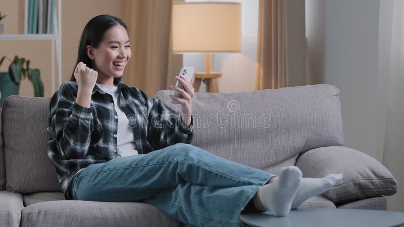 Mulher asiática sentada no sofá relaxando em casa no sofá jogando jogos móveis ganha nova mensagem de oferta de emprego online
