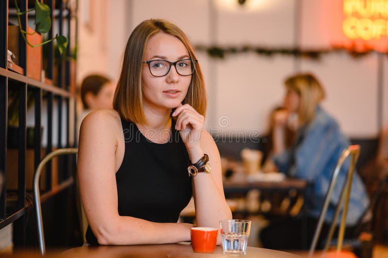 Mulher atrativa bonita em vidros pretos Menina feliz do negócio que trabalha em um café, sentando-se na tabela fotografia de stock Mulher atrativa bonita em vidros pretos Menina feliz do negócio que trabalha em um café, sentando-se na tabela fotografia de stock