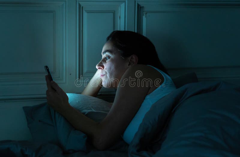 Mulher atrativa do latino dedicada ao telefone celular e ao Internet tarde em nigh na cama que olha sem sono fotografia de stock Mulher atrativa do latino dedicada ao telefone celular e ao Internet tarde em nigh na cama que olha sem sono fotografia de stock
