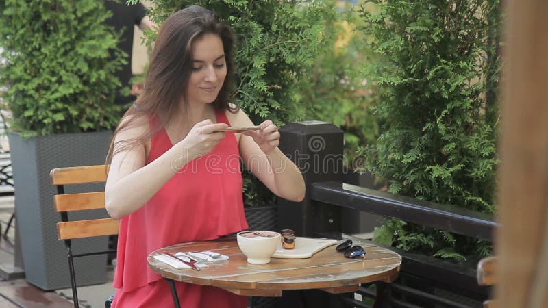 A mulher atrativa toma imagens do alimento no telefone no café do verão