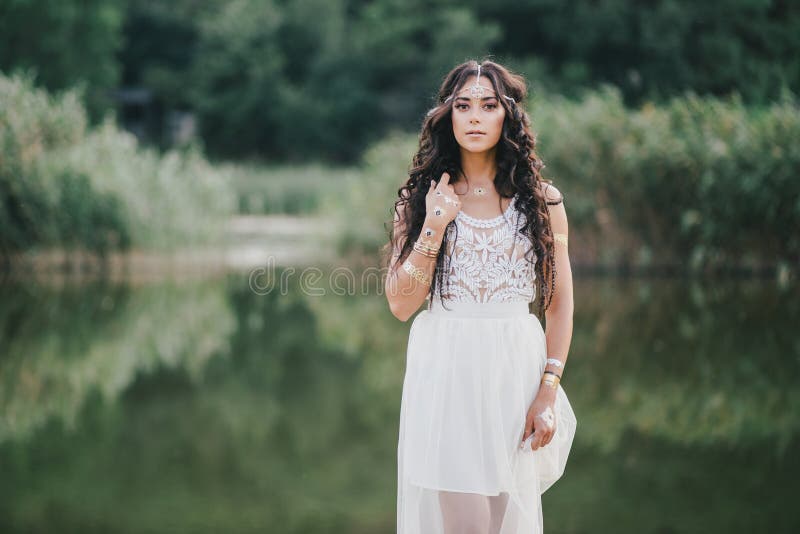 Beautiful young woman with long curly hair dressed in boho style dress posing near lake. Beautiful young woman with long curly hair dressed in boho style dress posing near lake