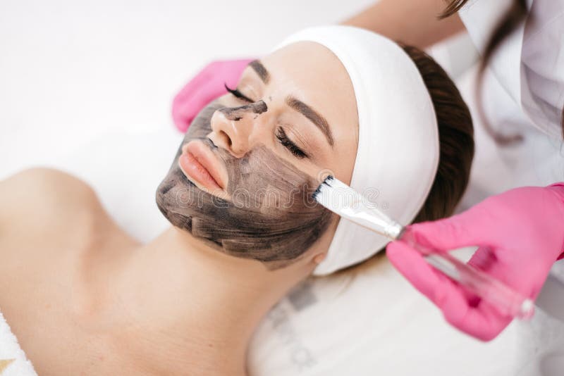 Mulher bonita de relaxamento com composição natural no salão de beleza dos termas As mãos do esteticista que aplicam a máscara pr fotografia de stock Mulher bonita de relaxamento com composição natural no salão de beleza dos termas As mãos do esteticista que aplicam a máscara pr fotografia de stock
