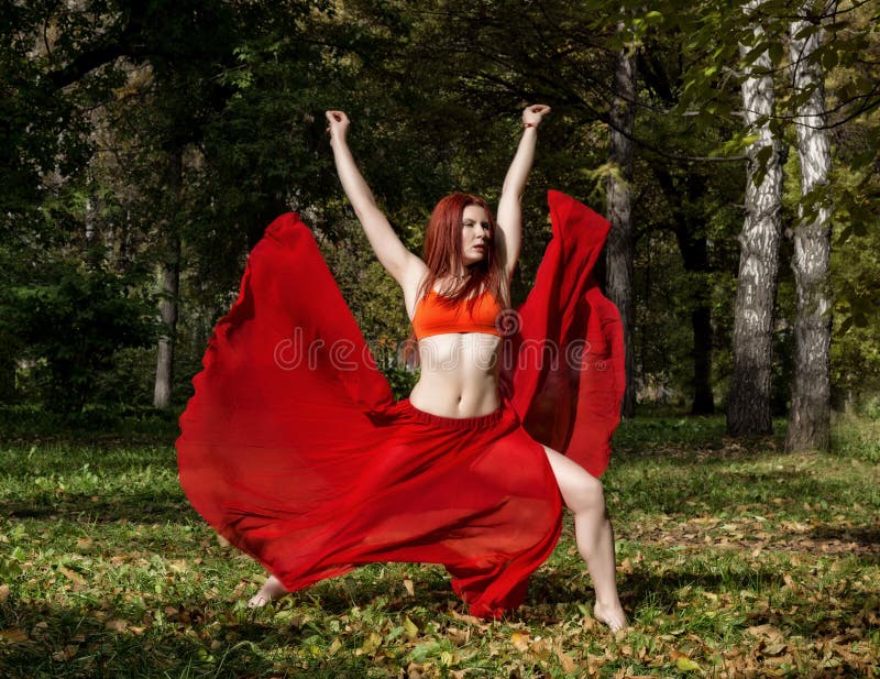 Mulher bonita do ruivo na dança vermelha do vestido em uma floresta do outono imagens de stock Mulher bonita do ruivo na dança vermelha do vestido em uma floresta do outono imagens de stock
