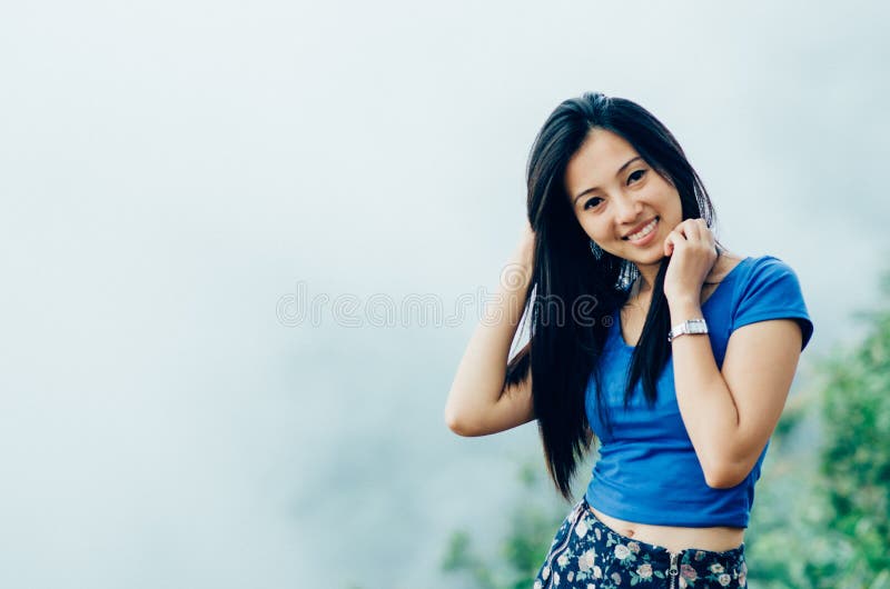 Mulher bonita nova asiática em um t-shirt azul em um penhasco de um mo imagens de stock royalty free Mulher bonita nova asiática em um t-shirt azul em um penhasco de um mo imagens de stock royalty free