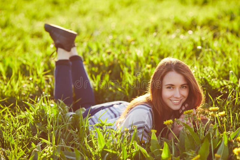 A mulher bonita nova do ruivo senta-se em um prado verde, olhando a c?mera fotografia de stock royalty free A mulher bonita nova do ruivo senta-se em um prado verde, olhando a c?mera fotografia de stock royalty free