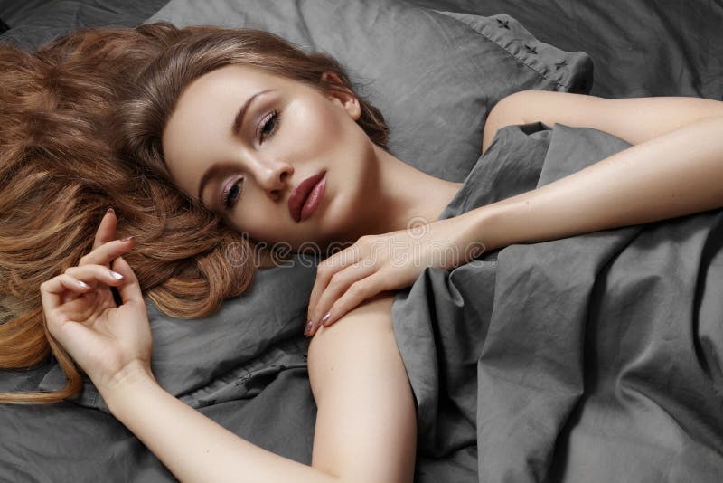 Mulher bonita que dorme ao encontrar-se na cama com conforto Sonhos doces Relaxamento modelo 'sexy' em folhas cinzentas
