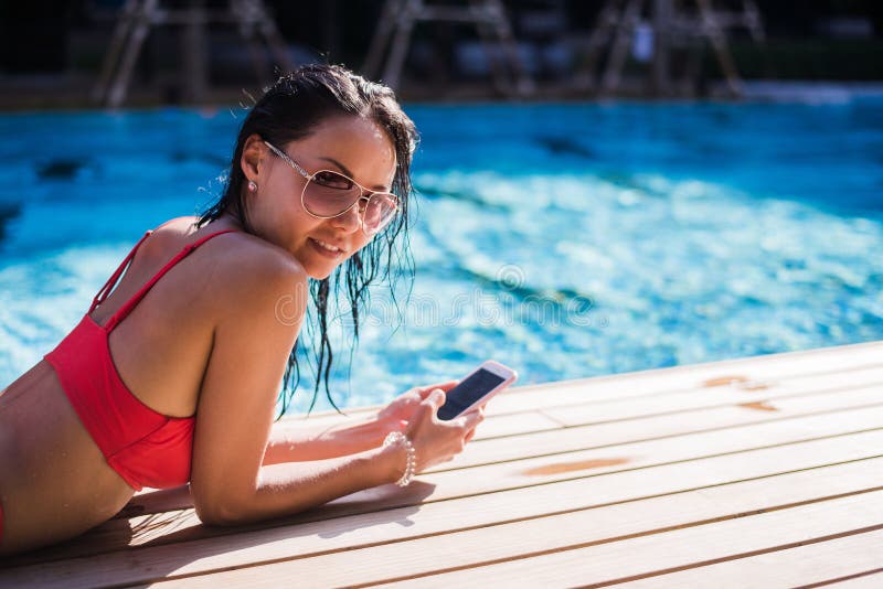Mulher bonita que inclina-se na piscina e que datilografa uma mensagem de texto no telefone celular fotografia de stock royalty free Mulher bonita que inclina-se na piscina e que datilografa uma mensagem de texto no telefone celular fotografia de stock royalty free