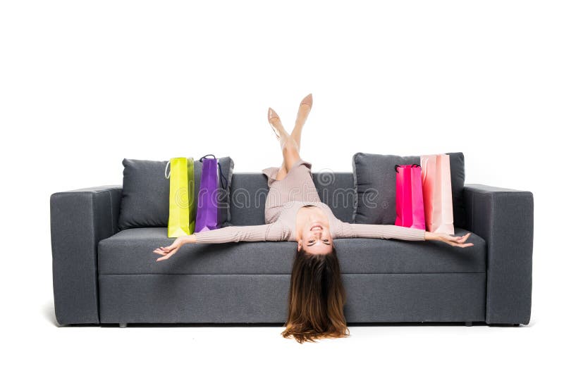 A mulher bonita que senta no sofá com muitos o saco de compras em torno da atuação alegre e feliz com braços espalhou largamente imagens de stock royalty free A mulher bonita que senta no sofá com muitos o saco de compras em torno da atuação alegre e feliz com braços espalhou largamente imagens de stock royalty free