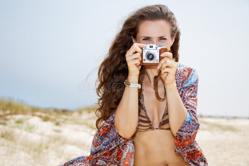 Mulher boêmia que toma fotos com a câmera retro da foto na praia