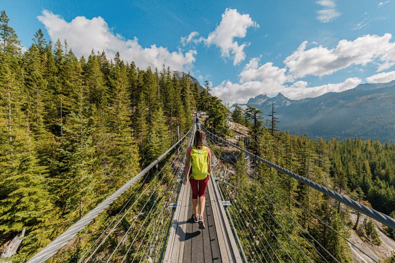 Mulher caminhando em montanhas cruzando a ponte suspensa sobre pés com visões surpreendentes. conceito de turismo canadense do bri
