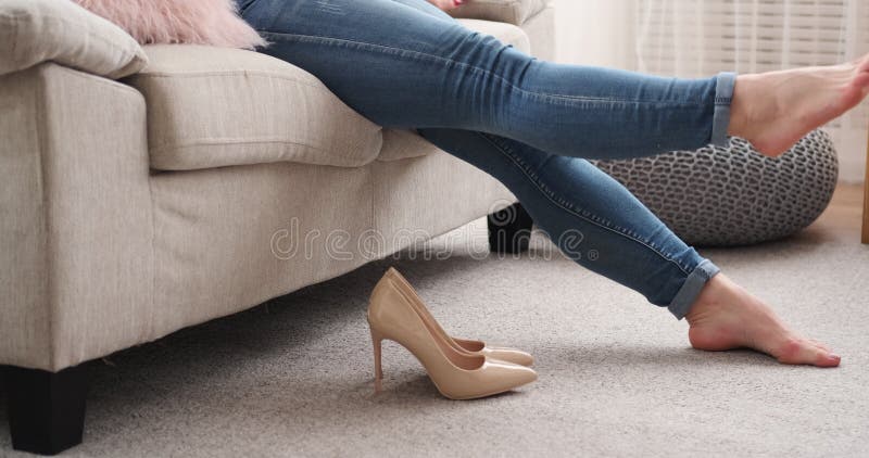 Mulher cansado que remove os stilettoes e que relaxa no sofá