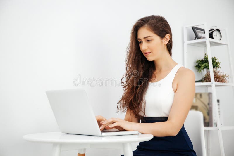 Mulher caucasiano bonita que trabalha no portátil na mesa branca sobre o fundo branco com espaço da cópia imagem de stock Mulher caucasiano bonita que trabalha no portátil na mesa branca sobre o fundo branco com espaço da cópia imagem de stock