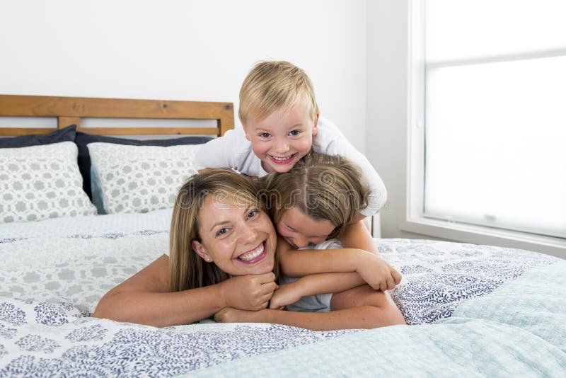 Mulher caucasiano loura nova que encontra-se na cama junto com seus jogo de riso velho anos pequenos do filho do doce 3 e 7 e da foto de stock Mulher caucasiano loura nova que encontra-se na cama junto com seus jogo de riso velho anos pequenos do filho do doce 3 e 7 e da foto de stock