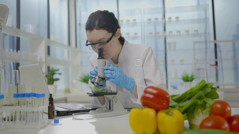 Mulher cientista olha pelo microscópio contra o fundo de vegetais frescos