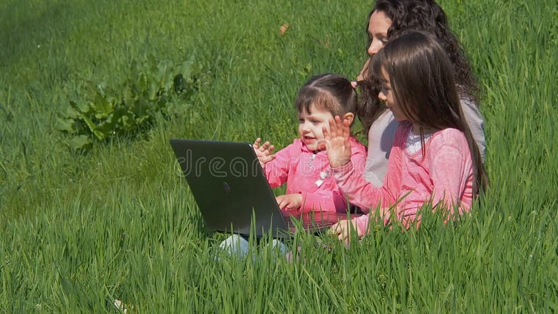 Mulher com as crianças na natureza com portátil Mamã e filhas no gramado verde Crianças no rosa Família feliz na natureza em um s