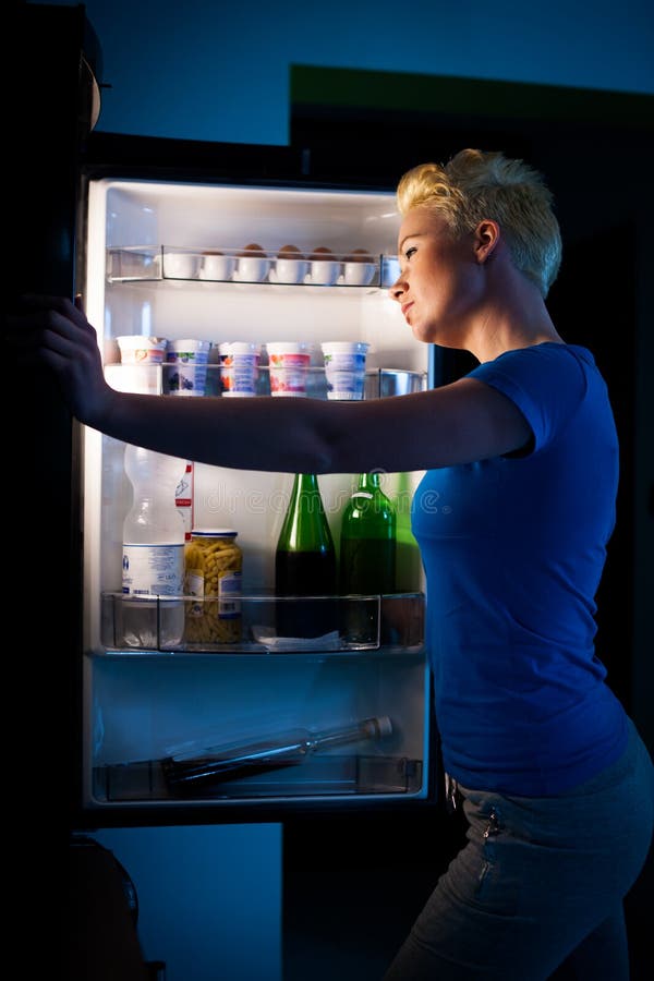 Mulher com fome que procura pelo alimento no refregirator na noite foto de stock Mulher com fome que procura pelo alimento no refregirator na noite foto de stock