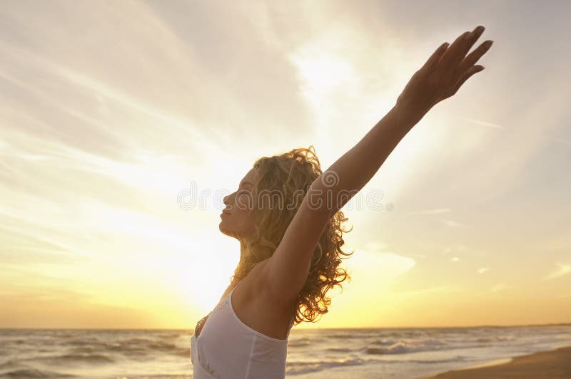 Side view of young woman with hands raised meditating at beach. Side view of young woman with hands raised meditating at beach