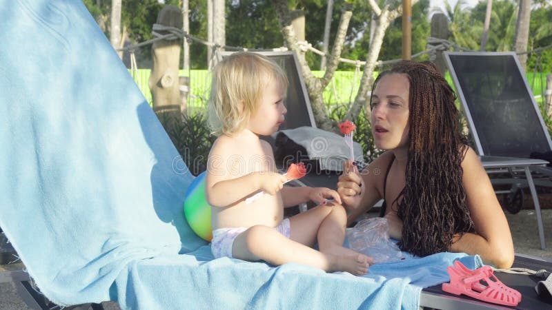 Mulher com a menina que come a melancia na praia