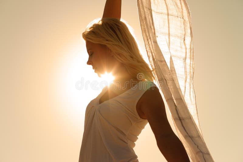 Woman with white scarf being backlit by the sun standing in the wind feeling happy and balanced. Woman with white scarf being backlit by the sun standing in the wind feeling happy and balanced