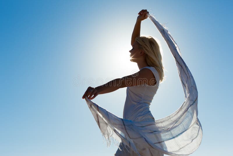 Woman with white scarf being backlit by the sun standing in the wind feeling happy and balanced. Woman with white scarf being backlit by the sun standing in the wind feeling happy and balanced