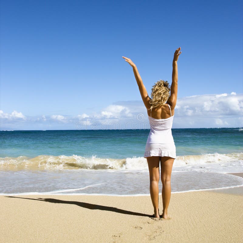 Pretty young woman standing on Maui, Hawaii beach with arms raised into air looking out towards ocean. Pretty young woman standing on Maui, Hawaii beach with arms raised into air looking out towards ocean.