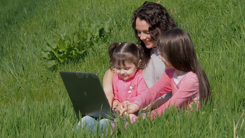 Mulher com portátil e crianças na grama verde Mamã e filhas no parque A família está falando no skype