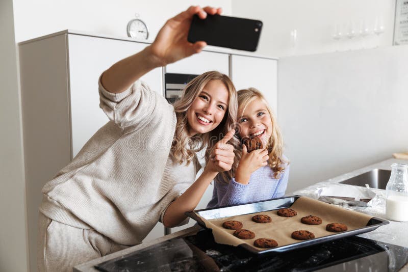 Mulher com sua da irmã mais nova cozinha dentro em casa que cozinha a padaria dos sweeties para tomar uma foto pelo telefone imagens de stock royalty free Mulher com sua da irmã mais nova cozinha dentro em casa que cozinha a padaria dos sweeties para tomar uma foto pelo telefone imagens de stock royalty free