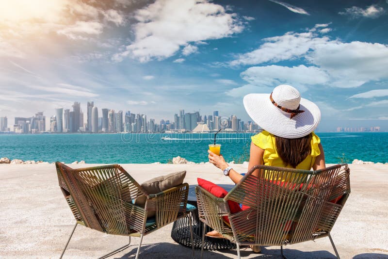 A mulher com um suco em sua mão aprecia a vista à skyline de Doha, Catar fotografia de stock royalty free A mulher com um suco em sua mão aprecia a vista à skyline de Doha, Catar fotografia de stock royalty free