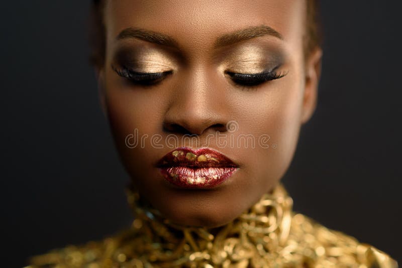 Mulher consideravelmente africana dos jovens, com o cabelo recolhido no penteado e na composição sensível do ouro, levantando no imagens de stock royalty free Mulher consideravelmente africana dos jovens, com o cabelo recolhido no penteado e na composição sensível do ouro, levantando no imagens de stock royalty free