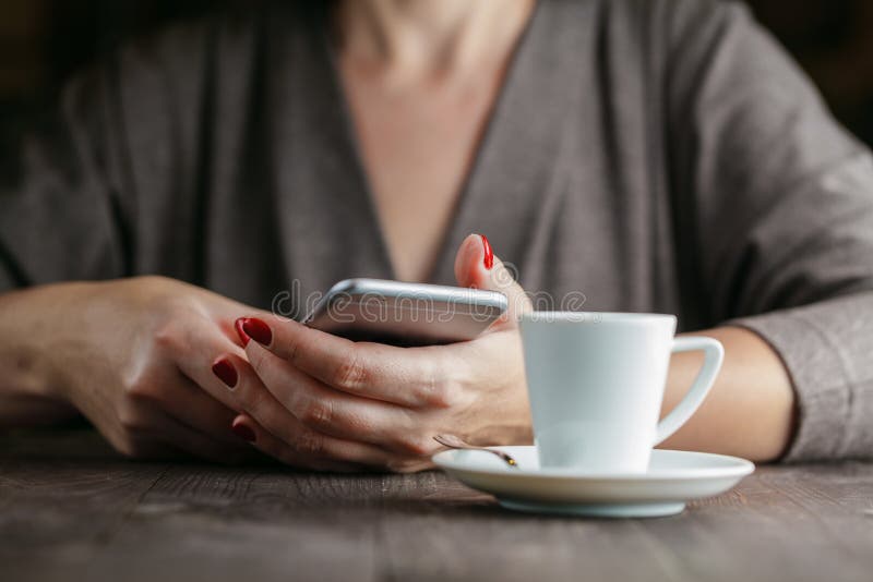 Mulher da mão que guarda o telefone e a xícara de café foto de stock Mulher da mão que guarda o telefone e a xícara de café foto de stock