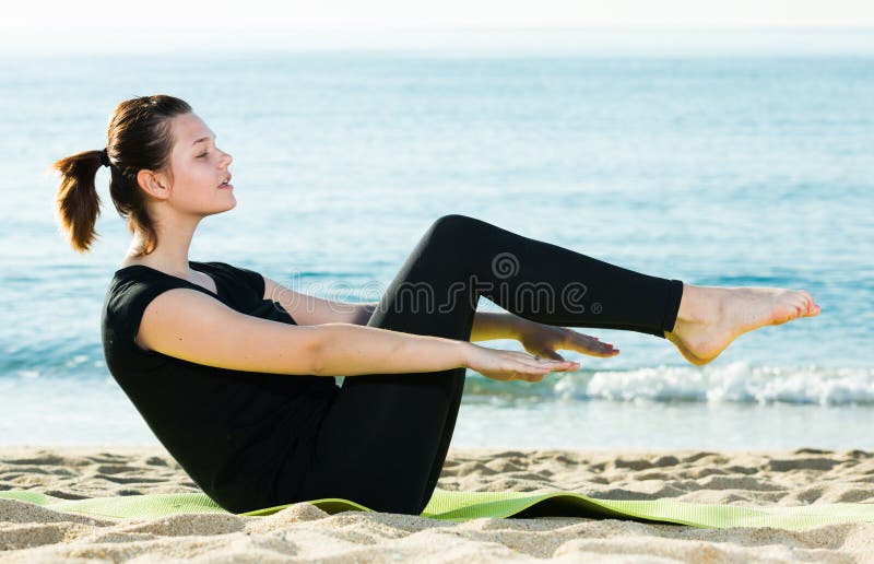 Female 20-30 years old is practicing yoga in black T-shirt on the beach near sea. Female 20-30 years old is practicing yoga in black T-shirt on the beach near sea.