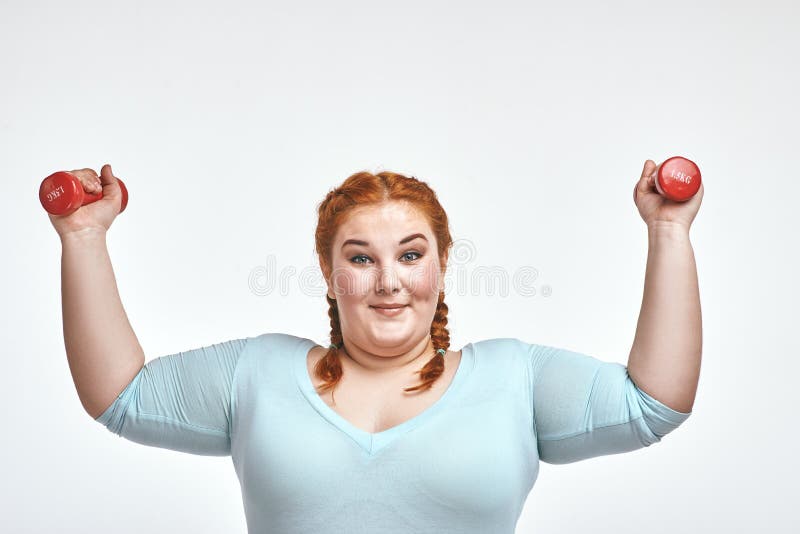 A mulher de cabelo, carnudo vermelha engraçada é de sorriso e guardando pesos imagens de stock royalty free A mulher de cabelo, carnudo vermelha engraçada é de sorriso e guardando pesos imagens de stock royalty free