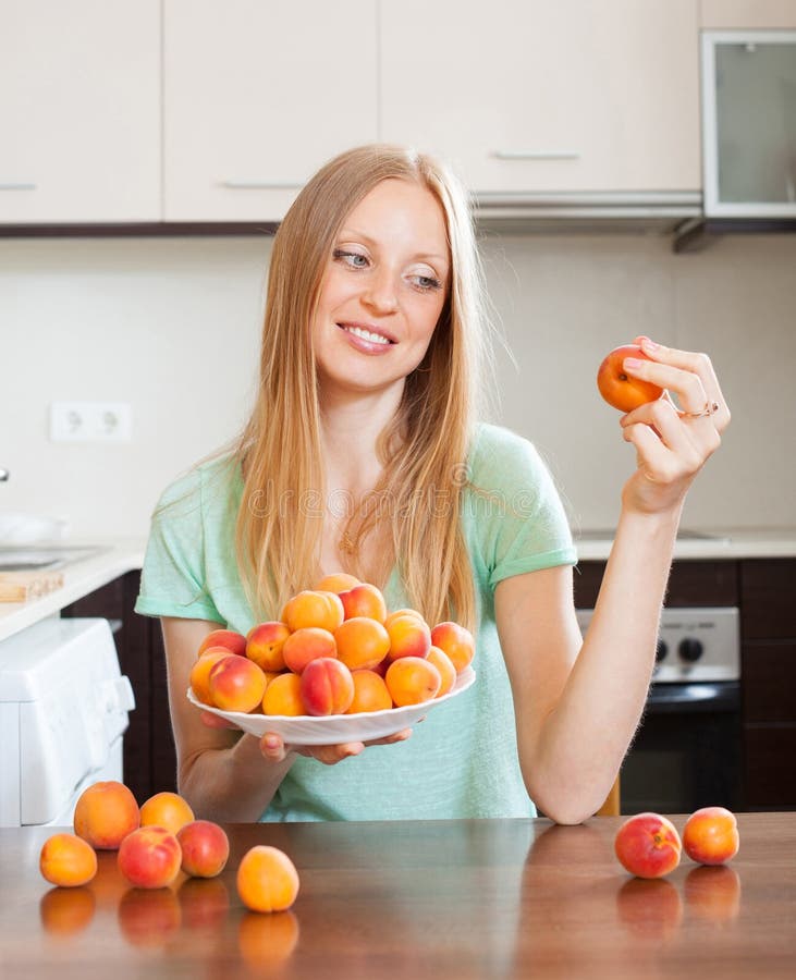 Mulher de cabelos compridos loura que come abricós na cozinha home foto de stock Mulher de cabelos compridos loura que come abricós na cozinha home foto de stock