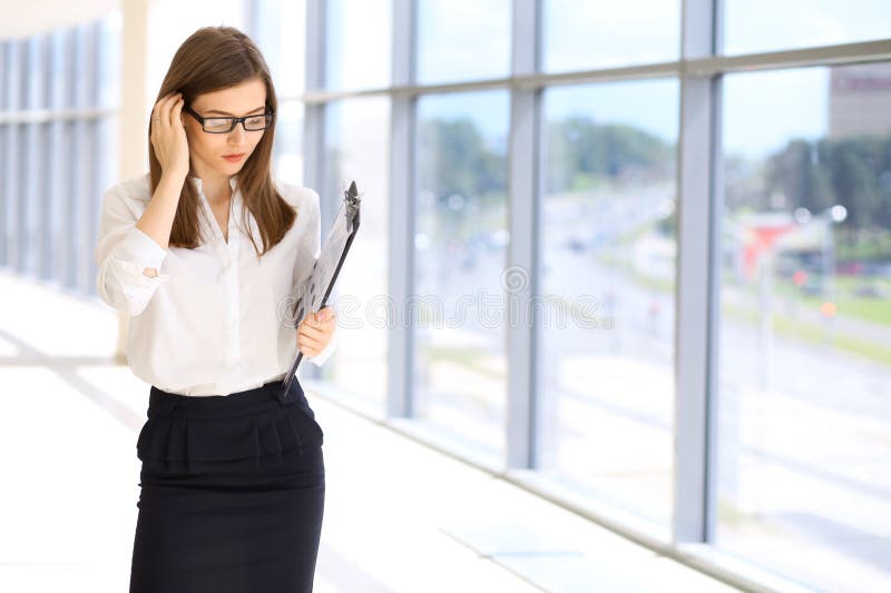 Mulher de negócio moderna que está e que mantém uma prancheta no escritório imagem de stock Mulher de negócio moderna que está e que mantém uma prancheta no escritório imagem de stock