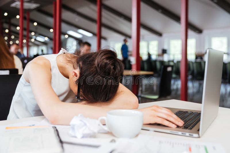 Mulher de negócio nova desgastada esgotada que dorme na tabela no local de trabalho imagens de stock royalty free Mulher de negócio nova desgastada esgotada que dorme na tabela no local de trabalho imagens de stock royalty free