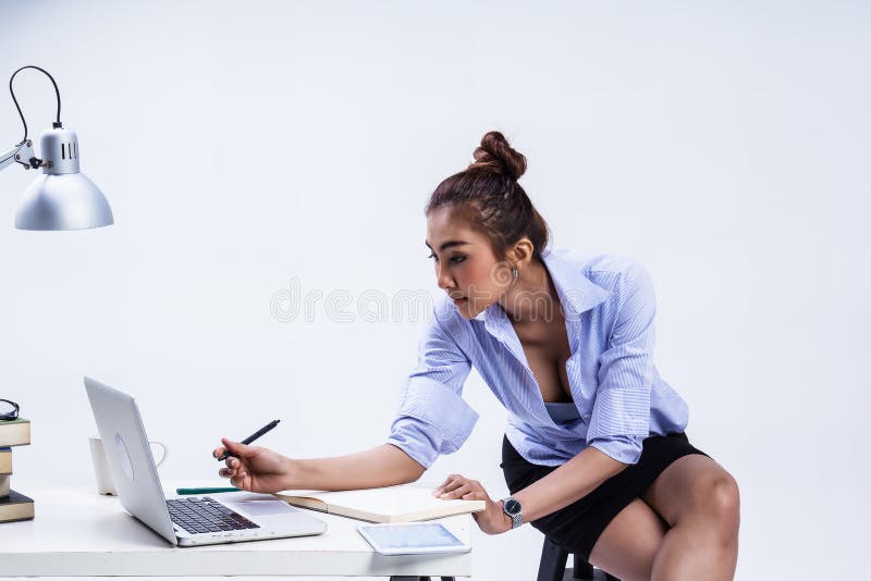 A mulher de negócio que trabalha no escritório, está sentando-se na cadeira preta, pena da posse à disposição, olhando o portátil imagem de stock royalty free A mulher de negócio que trabalha no escritório, está sentando-se na cadeira preta, pena da posse à disposição, olhando o portátil imagem de stock royalty free