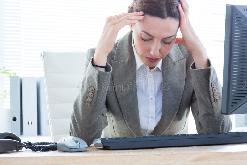 Mulher de negócio virada com cabeça nas mãos na frente do computador no escritório foto de stock Mulher de negócio virada com cabeça nas mãos na frente do computador no escritório foto de stock