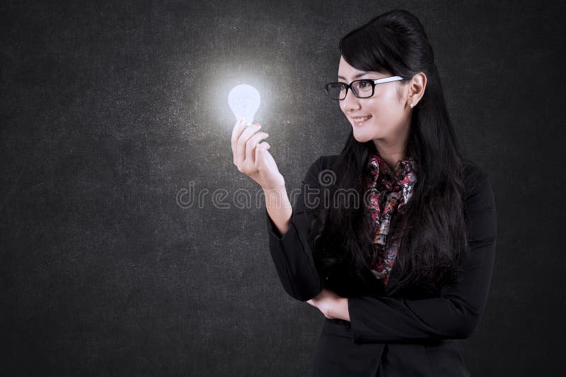 Mulher de negócios asiática que olha um bulbo brilhante fotos de stock Mulher de negócios asiática que olha um bulbo brilhante fotos de stock