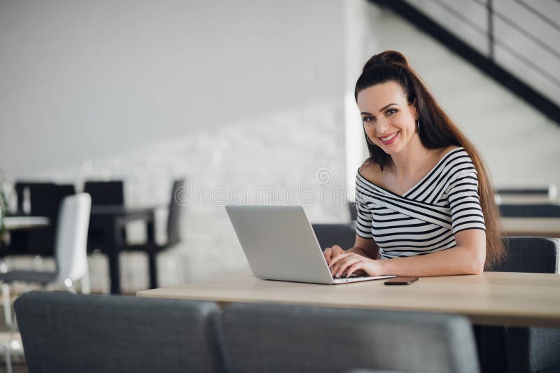 Mulher de negócios elegante e alegre A mulher bonita nova alegre está olhando a câmera com sorriso ao sentar-se nela imagem de stock royalty free Mulher de negócios elegante e alegre A mulher bonita nova alegre está olhando a câmera com sorriso ao sentar-se nela imagem de stock royalty free