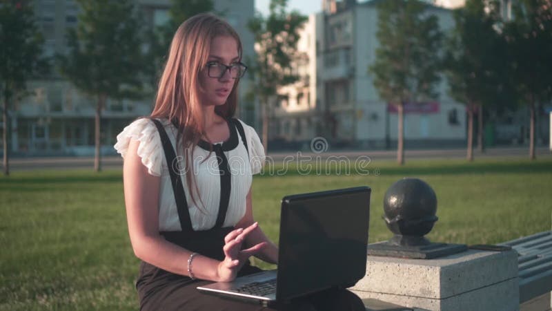 Mulher de negócios em camisa branca e óculos senta em um banco, trabalha em um laptop A garota não está feliz com o trabalho e co