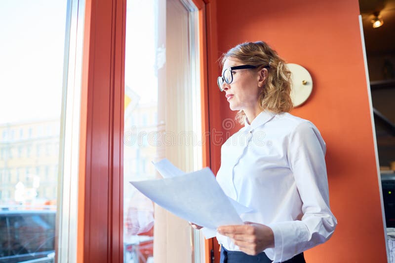 Mulher de negócios formal com o papel que olha na janela imagem de stock Mulher de negócios formal com o papel que olha na janela imagem de stock