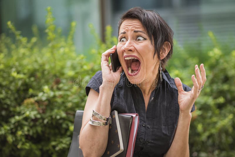 Shocked mature corporate woman receiving terrible news over her cell phone. Shocked mature corporate woman receiving terrible news over her cell phone
