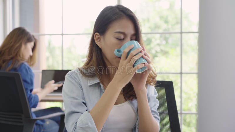 Mulher de negócios nova asiática alegre que senta-se no café bebendo do escritório