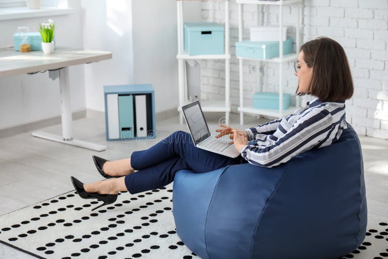 Mulher de negócios nova com o portátil que senta-se na cadeira do beanbag no escritório fotos de stock Mulher de negócios nova com o portátil que senta-se na cadeira do beanbag no escritório fotos de stock