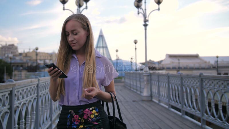 Mulher de negócios nova que anda na ponte com telefone