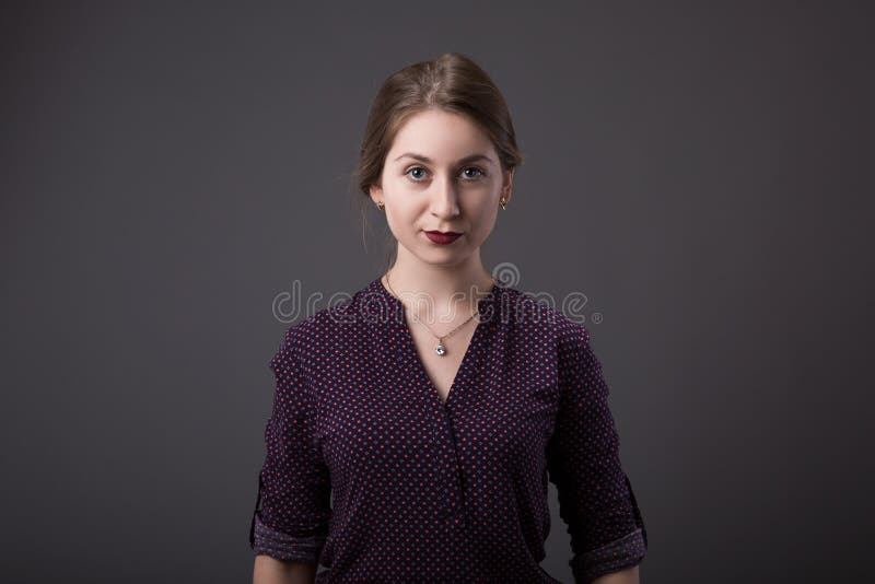 Mulher de negócios nova à moda com uma expressão amigável que olha diretamente na câmera, close up de sua cara em um cinza imagem de stock Mulher de negócios nova à moda com uma expressão amigável que olha diretamente na câmera, close up de sua cara em um cinza imagem de stock