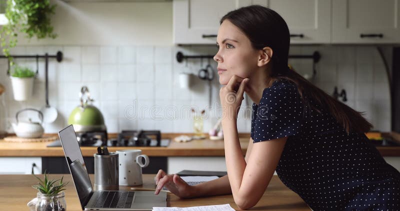Mulher de pé na cozinha usa laptop considerar solução para problemas