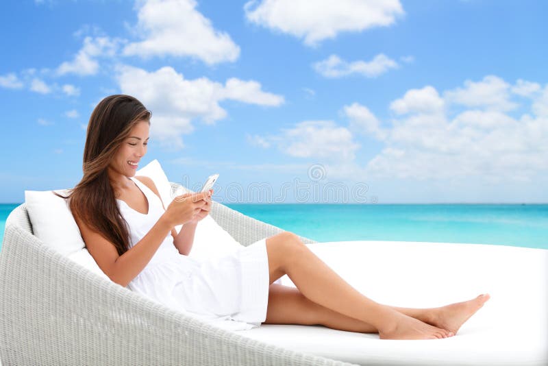 Mulher de Smartphone que usa o telefone app no sofá da cama da praia foto de stock Mulher de Smartphone que usa o telefone app no sofá da cama da praia foto de stock