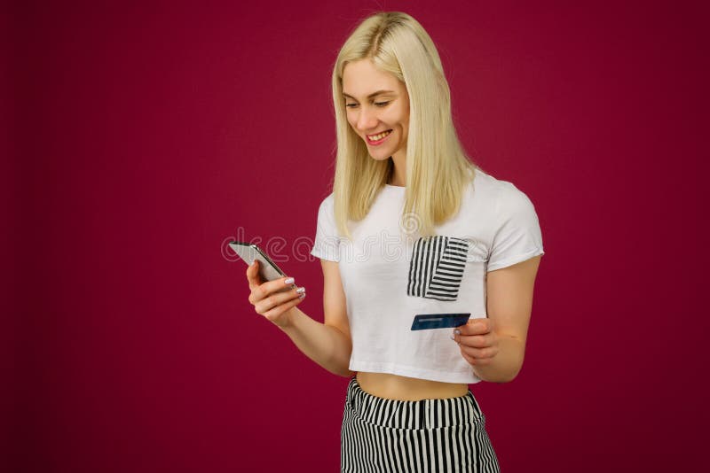 A mulher de sorriso nova compra em linha Guarda um smartphone e um cartão de crédito à disposição fotos de stock A mulher de sorriso nova compra em linha Guarda um smartphone e um cartão de crédito à disposição fotos de stock